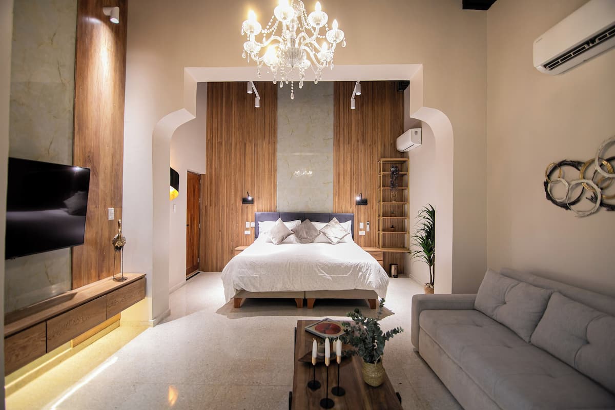 A modern bedroom with a large bed, a chandelier, a TV, and a sofa.