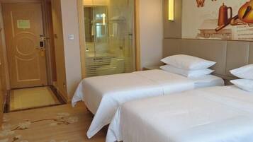 A hotel room with two single beds, a wooden door, a glass shower enclosure, and a wall with a coffee cup and butterflies.