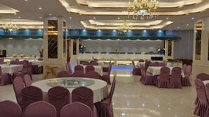 A banquet hall with round tables and purple chairs, a stage with a blue backdrop, and chandeliers. - Vienna Hotel (Yudu Railway Station) (Yudu)
