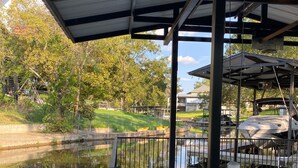 A covered dock area with a concrete walkway, metal railing, and a view of a pond with reflections. - Waterfront 5/3 roomy home, constant level Lake LBJ, jet ski ramp & covered porch (Kingsland)