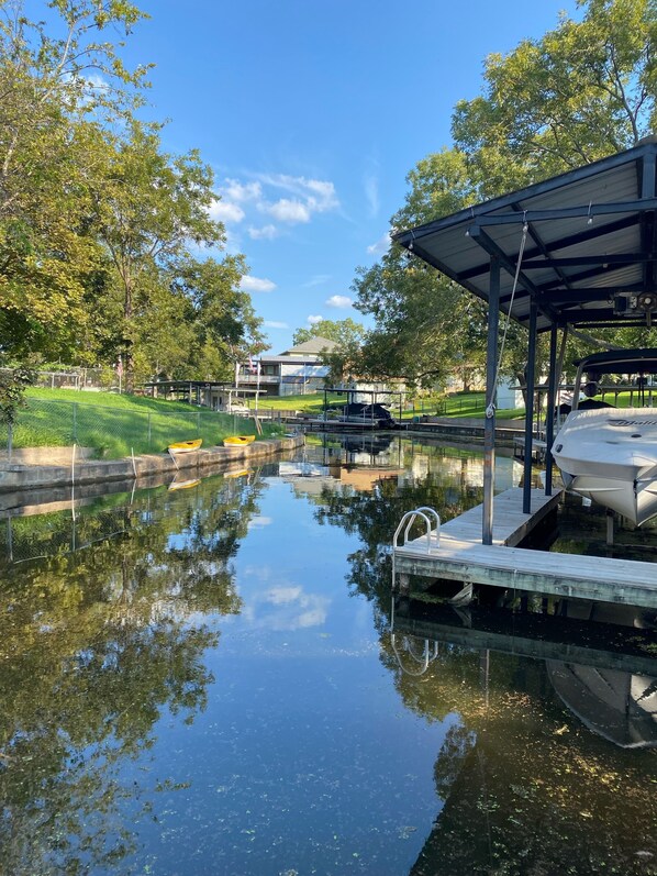 A calm water body with boats docked, surrounded by greenery and a building in the background.