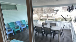 A deck with a table and chairs, a fan, and a view of a building across a body of water. - Waterfront 5/3 roomy home, constant level Lake LBJ, jet ski ramp & covered porch (Kingsland)