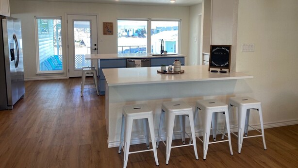 A modern kitchen with a central island, white bar stools, a refrigerator, and a chalkboard sign. - Waterfront 5/3 roomy home, constant level Lake LBJ, jet ski ramp & covered porch (Kingsland)