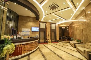 Un hall d’hôtel comprenant un comptoir d’accueil, un téléviseur, un tapis rouge et un espace détente avec un canapé et des fauteuils.