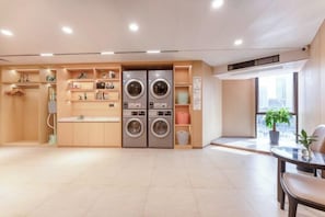 A modern laundry room with built-in washers and dryers, shelves with toiletries, and a view of the city through large windows. - Jiangmen Park Lane Yiju Hotel (Wuyi University Baishi) (Jiangmen)