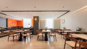 A modern dining area with multiple tables and chairs, a kitchen in the background, and a bright, well-lit space. - Jiangmen Park Lane Yiju Hotel (Wuyi University Baishi) (Jiangmen)
