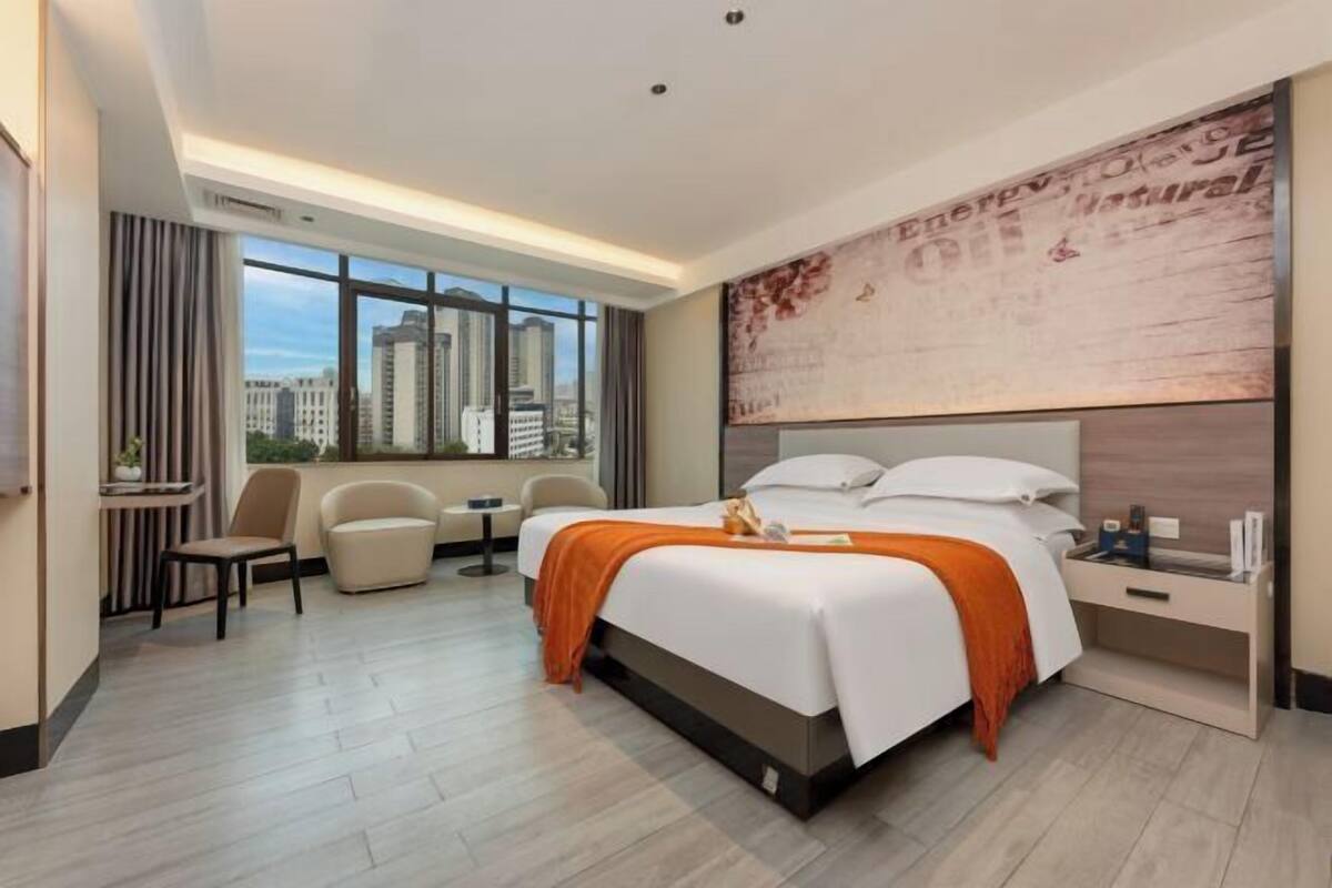 Habitación de hotel moderna con una cama grande, un escritorio, una silla y vistas a la ciudad.