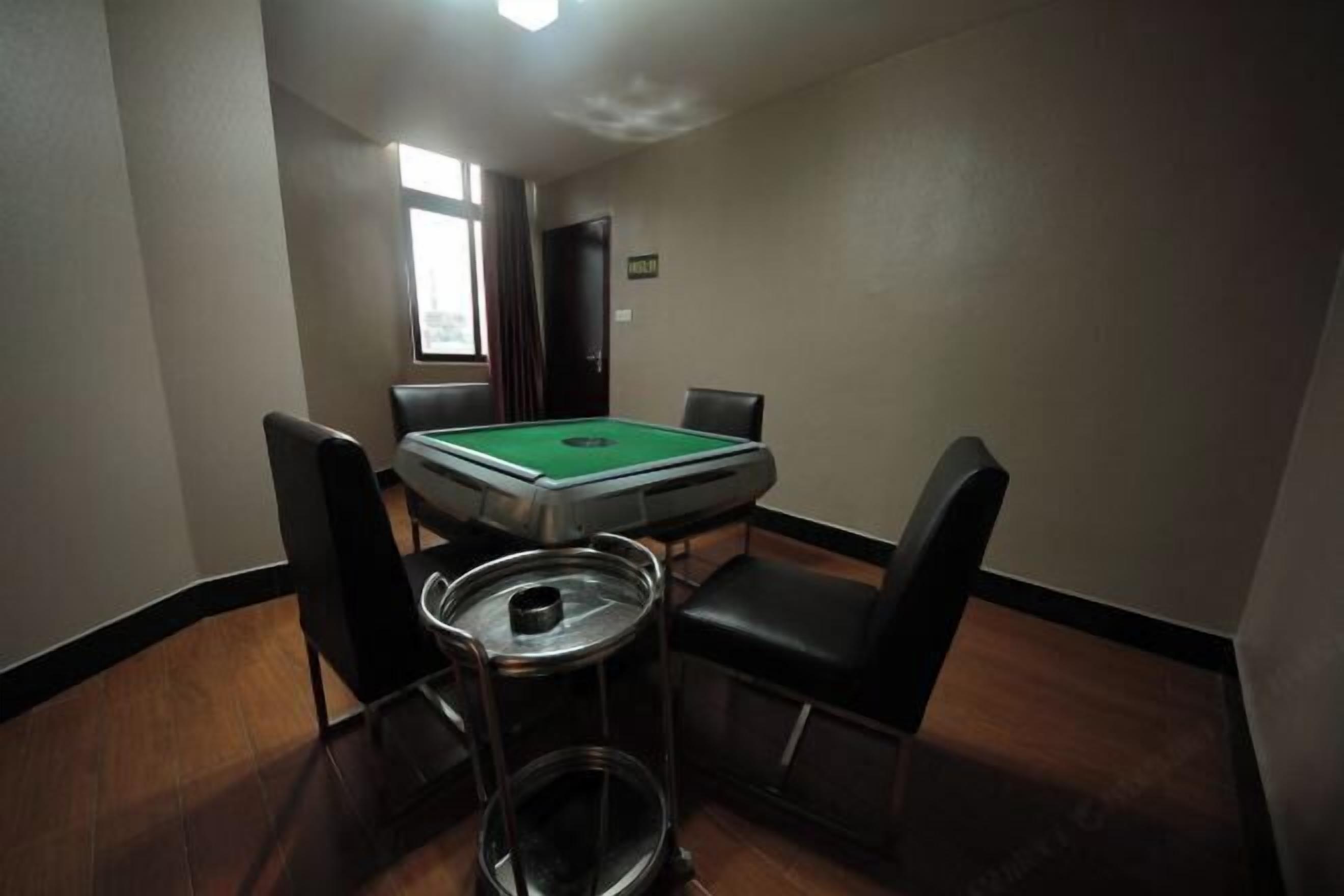 A room with a pool table, four chairs, a trash can, and a window.