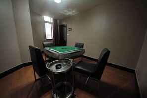 A room with a pool table, four chairs, a trash can, and a window.