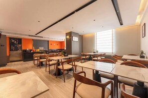 Un espace de restauration moderne avec plusieurs tables et chaises, une cuisine en arrière-plan et une grande fenêtre qui laisse entrer la lumière naturelle.