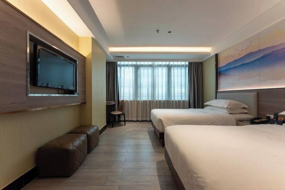 Habitación de hotel con dos camas, televisión, escritorio, silla y ventana con cortinas.