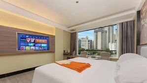 A hotel room with a large bed, a TV mounted on the wall, a desk, and a view of tall buildings. - Jiangmen Park Lane Yiju Hotel (Wuyi University Baishi) (Jiangmen)