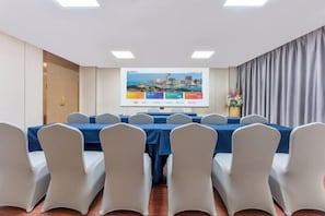 A conference room with a long table, white chairs, a projector screen, and a floral arrangement. - Jiangmen Park Lane Yiju Hotel (Wuyi University Baishi) (Jiangmen)