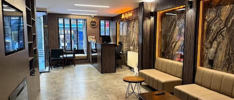 A hotel lobby with a reception desk, seating area, and a television.