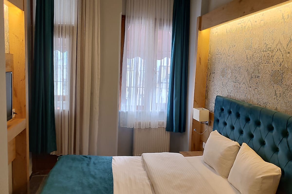 A bedroom with a bed, curtains, a headboard, and a wall with a textured pattern.