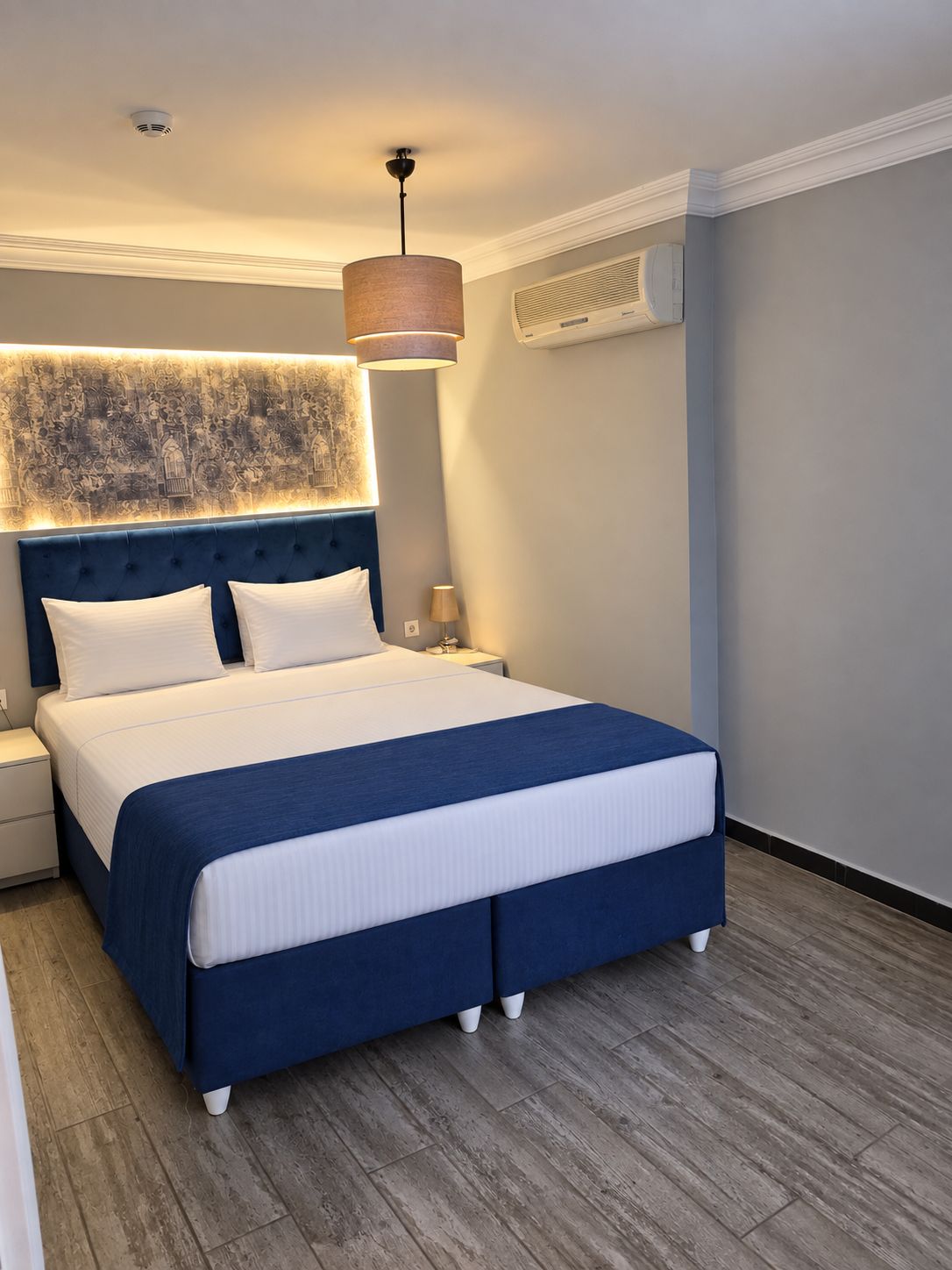 Un dormitorio moderno con una cama grande, una mesita de noche, un aire acondicionado instalado en la pared y una lámpara en el techo.