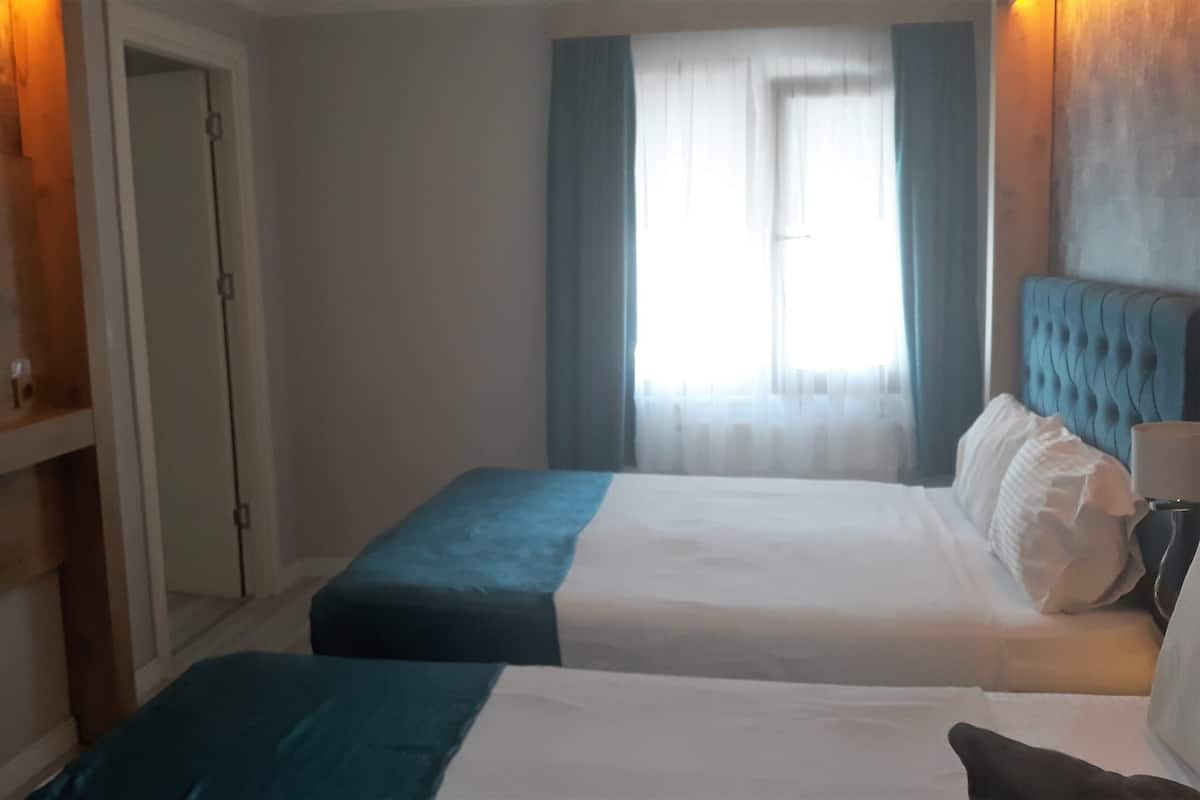 A hotel room with two beds, a television on the wall, and a window with curtains.