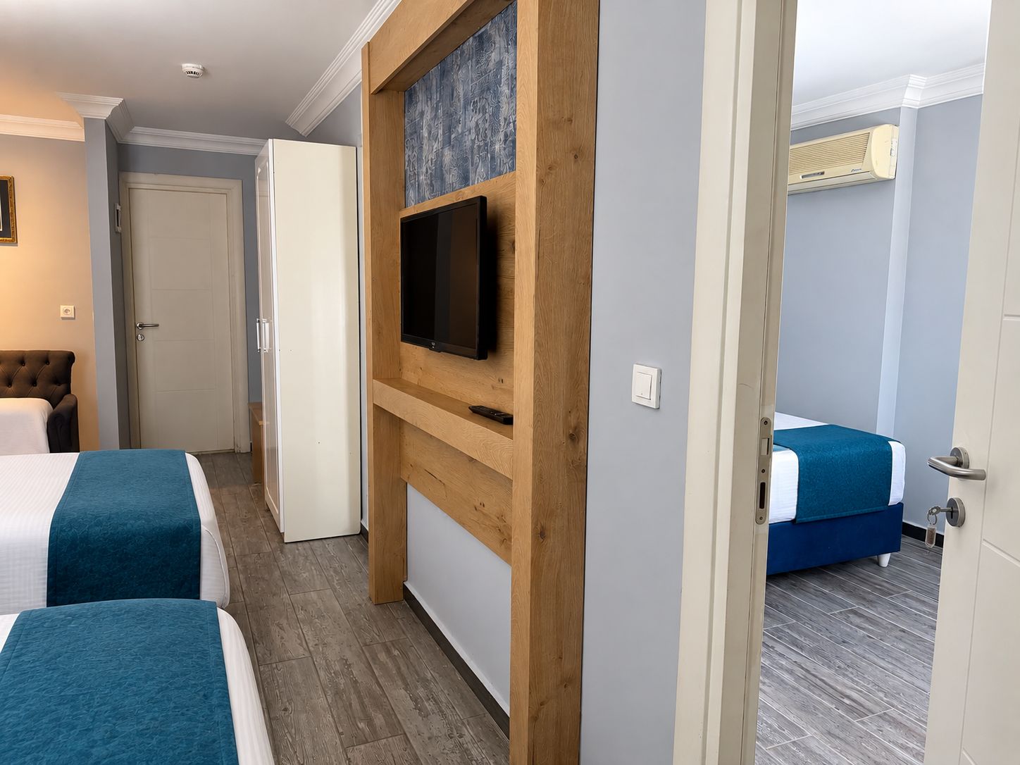 Et hotelværelse med to senge, et fjernsyn monteret på en træpanel, en dør og en aircondition-enhed.