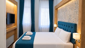 A hotel room with a large bed, a flat-screen TV, a wooden headboard, and a patterned wallpaper.