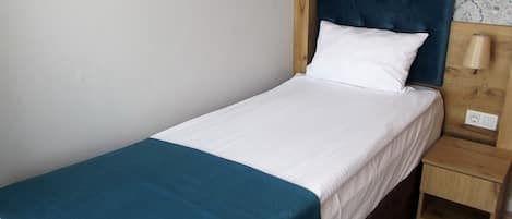 Una cama individual con colchón blanco y una manta turquesa.