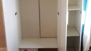 A walk-in closet with open doors, a hanging rod, and a small drawer unit.