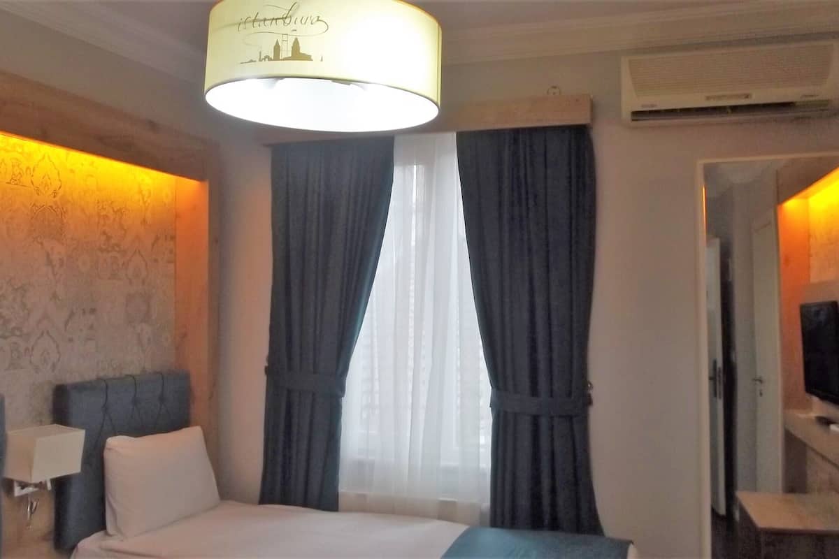 A hotel room with a bed, a nightstand, a lamp, a window with curtains, and an air conditioning unit.