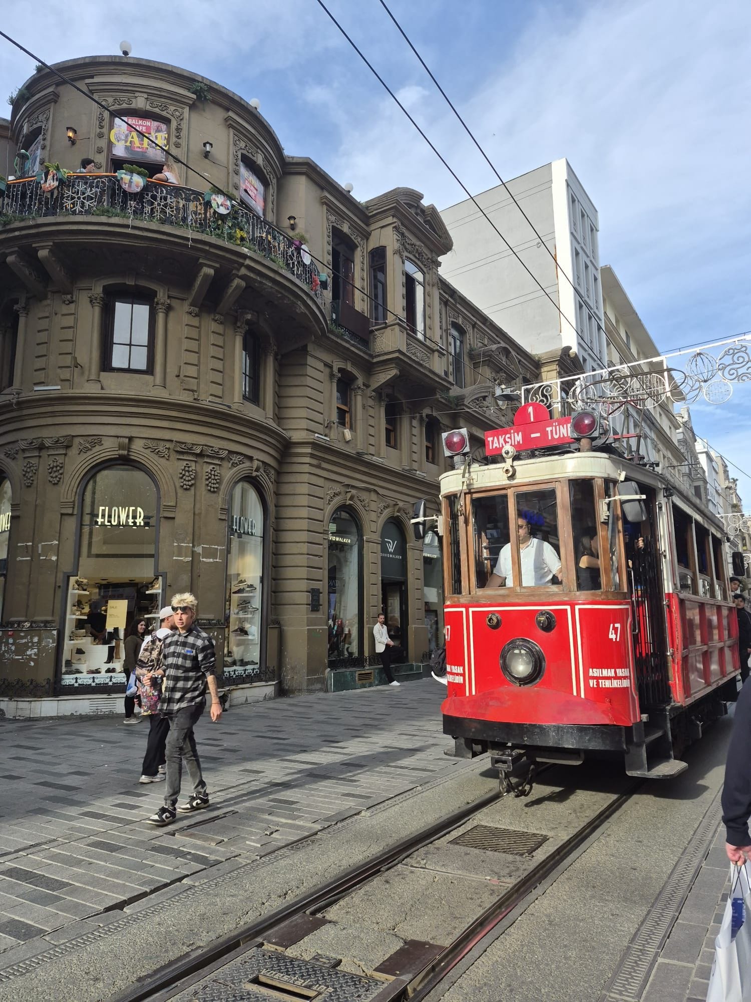 A tram with a red and white color scheme, a sign indicating it is route number 1, and a building with ornate architecture and a shop named 'FLOWER' in the background.