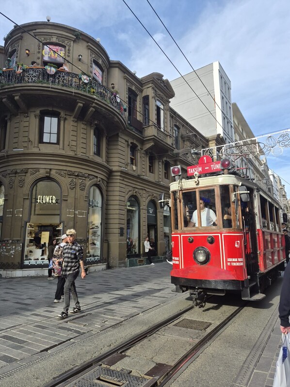 A tram with a red and white color scheme, a sign indicating it is route number 1, and a building with ornate architecture and a shop named 'FLOWER' in the background.