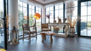 Ruime kamer met grote ramen, een houten vloer, twee stoelen, een tafel, een lamp en diverse decoratieve objecten.