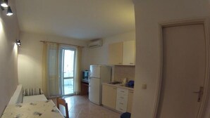 A compact kitchen with a dining area, a small refrigerator, and a window with curtains.