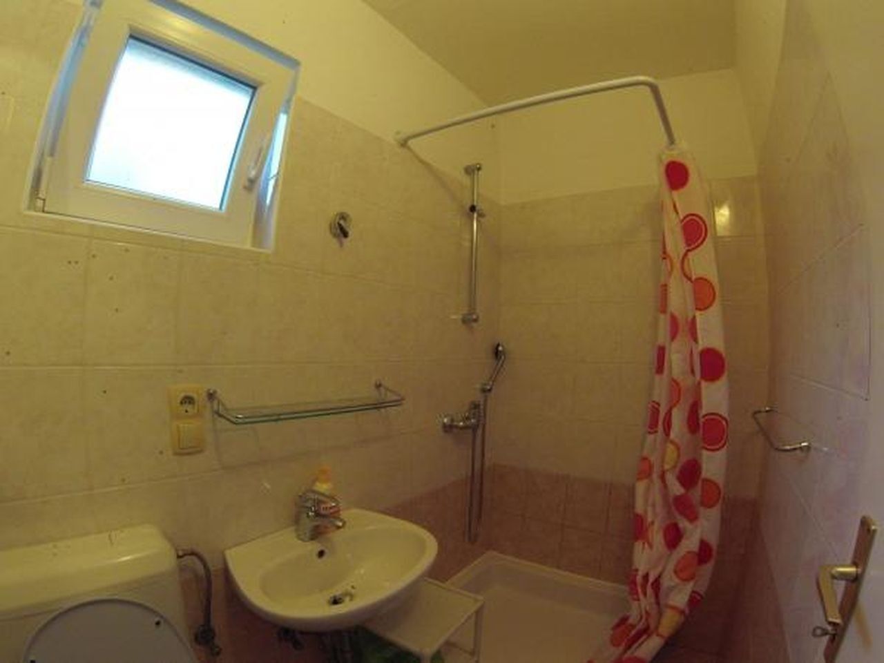A small bathroom with a window, a shower, a sink, and a toilet.
