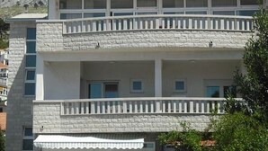 A two-story building with balconies, a stone facade, and a mountainous backdrop.