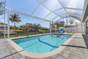 Una piscina limpida con una zona coperta, una bandiera e una palma sullo sfondo.