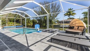 Piscina scoperta coperta con lettini e ombrellone, immersa nel verde e con vista su un corpo d'acqua.