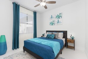 Una camera da letto con un letto, un comodino, una ventola a soffitto e opere d'arte alle pareti.