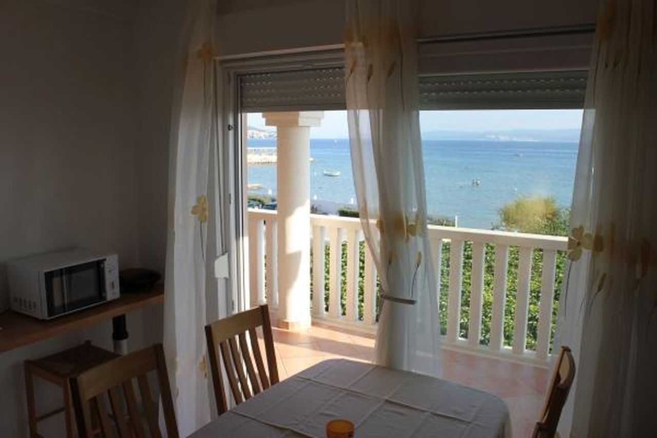 A balcony with a view of the sea, a table with a white tablecloth, and a microwave on a shelf.