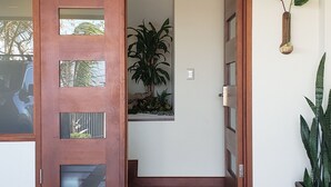 A wooden door with glass panels, a potted plant, and a wall-mounted vase with a sunflower. - Cozy Escazú Apartment with great view & location (Escazú)