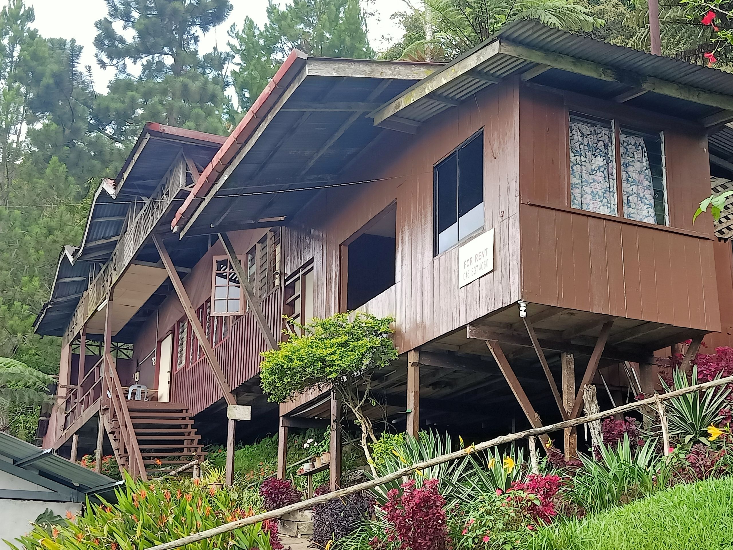 A wooden house with a balcony and a 'For Rent' sign.