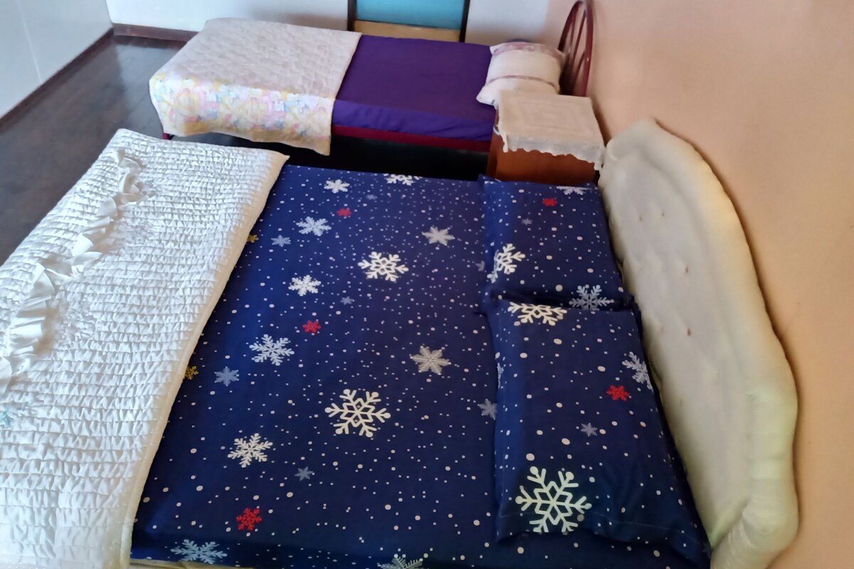 Een kamer met een bed belegd met een blauwe deken met sneeuwvlokken, een witte gebreide deken en een houten hoofdbord.