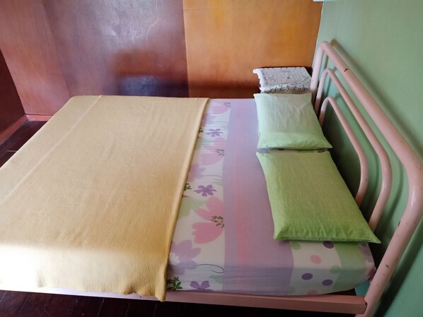Una cama con una colcha estampada con motivos florales y dos almohadas, un cabecero de madera y suelo de madera.