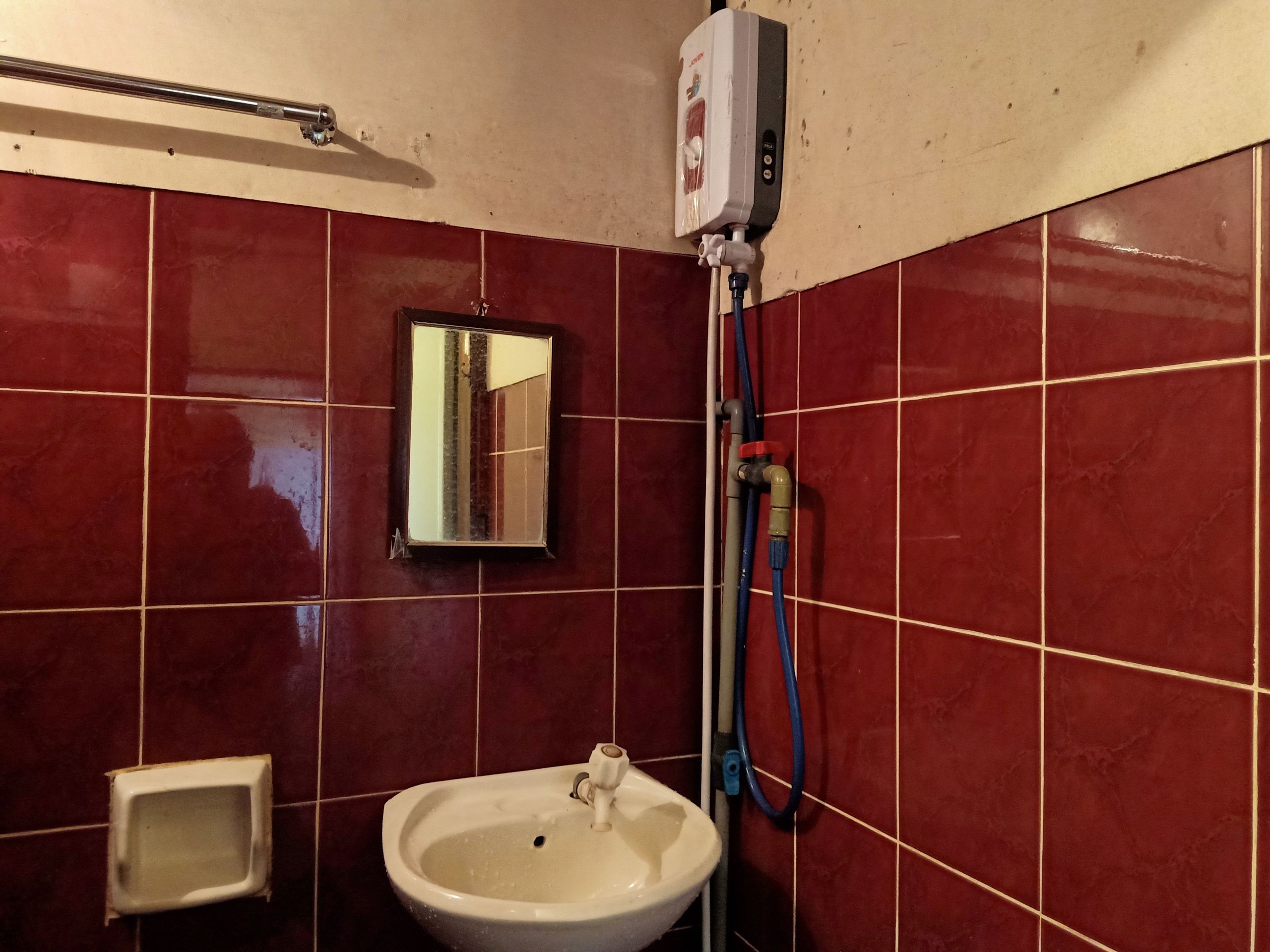 A bathroom with red tiles, a white sink, a mirror, and a hand dryer.