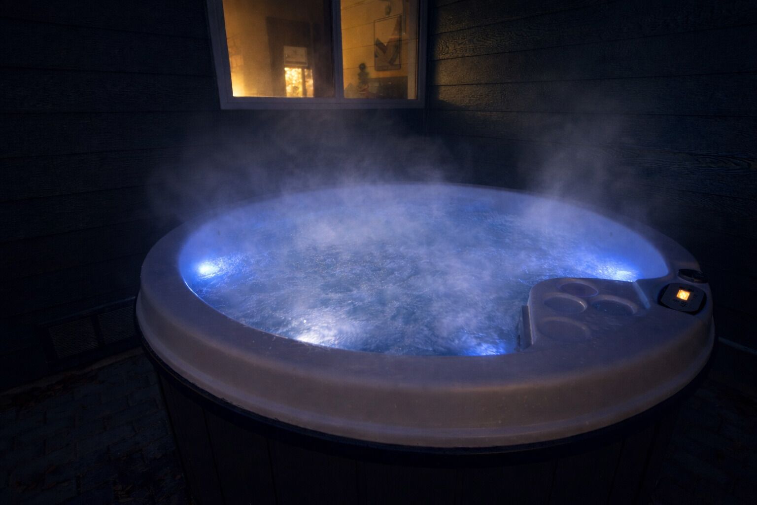 Ett bubbelbad med ånga som stiger upp från vattnet, omgivet av träväggar och ett fönster.