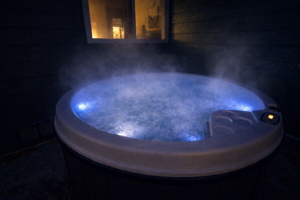 A hot tub with steam rising from the water, surrounded by wooden walls and a window.