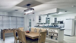 A modern kitchen with white cabinets, a wooden dining table with chairs, and a central island with a sink.