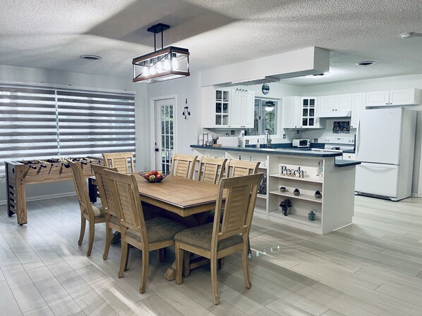 A modern kitchen with white cabinets, a wooden dining table with chairs, and a central island with a sink.