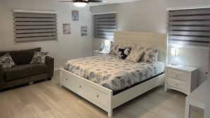 A bedroom with a bed, a nightstand, a bedside table, a ceiling fan, and a window with blinds.