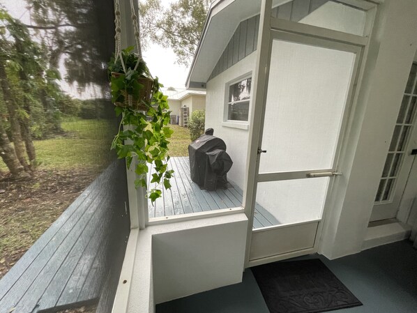 Een overdekte veranda met een deur, een klein raam en een zwart object op de vloer.
