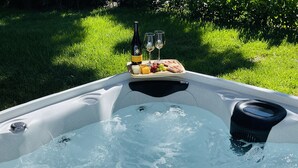 A hot tub with a table set for a meal, including a bottle of wine, glasses, and a tray of food.