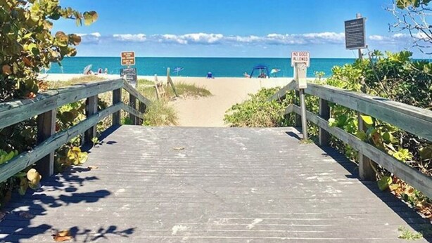 A wooden boardwalk leading to a beach with clear skies and calm waters.