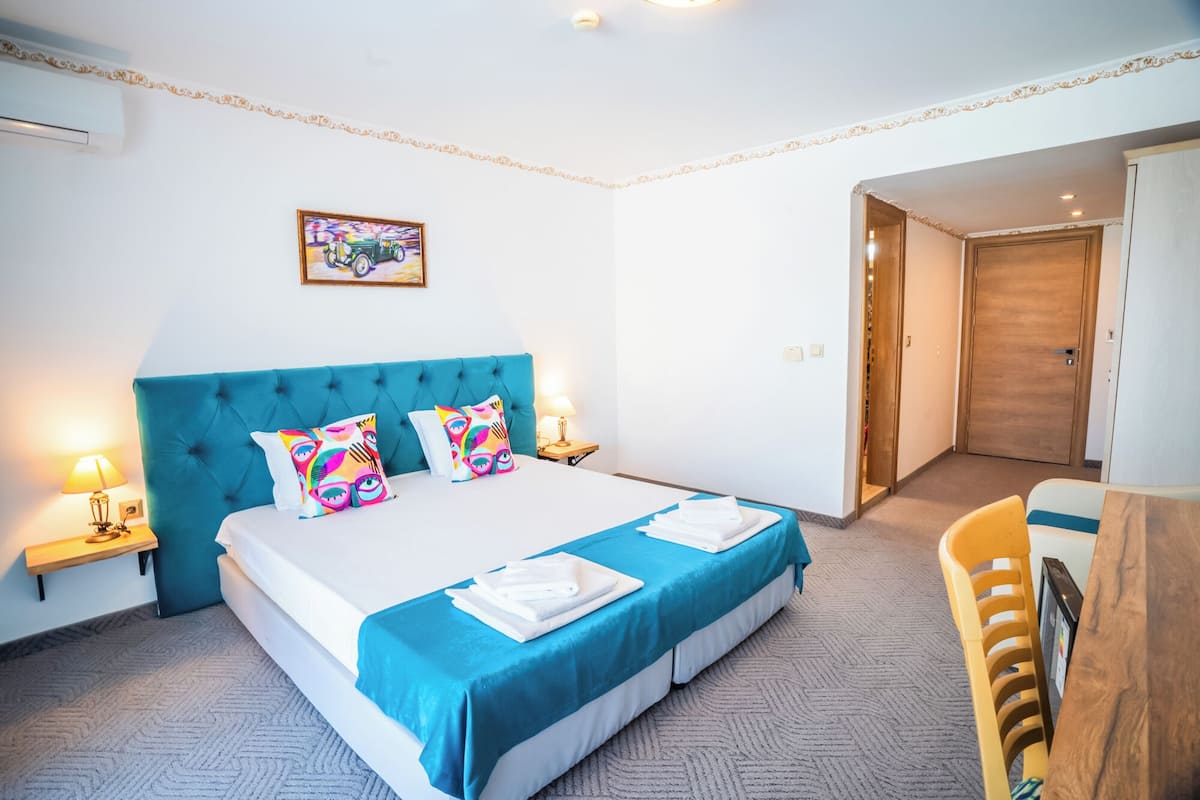 Een hotelkamer met een groot bed, een blauw hoofdbord, een kleurrijk kunstwerk aan de muur en een houten deur.